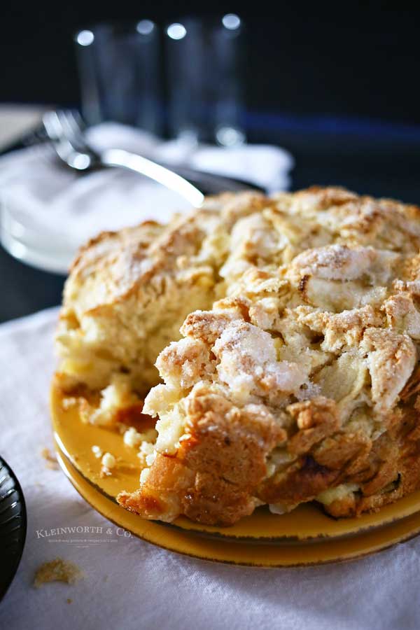 A close-up of a slice of Irish apple cake, lightly dusted with powdered sugar, showing the cake's dense crumb and chunks of apple, served on a plate.