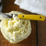 Overhead view of whipped butter with garlic and chives in a jar with a butter knife laying on top.