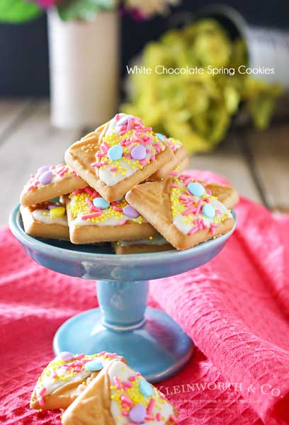 Looking for a quick little treat to serve at all your Easter gatherings? Creating cute treats like these White Chocolate Spring Cookies for Easter is easy. Simple shortbread cookies, white chocolate & Easter sprinkles is so much fun! These literally take about 15 minutes to make & everyone just loves them. People will think you slaved away in the kitchen for hours. They are an adorable Easter dessert that bring BIG smiles!