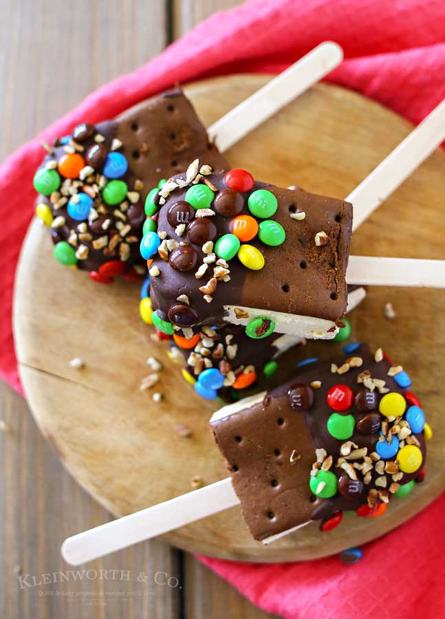 Ice Cream Sandwich Pops are an easy summer treat to make. Made with a simple ice cream sandwich, chocolate & decorations they are a perfect frozen treat. Make some for all of your celebrations, holidays & backyard BBQ's this summer. 