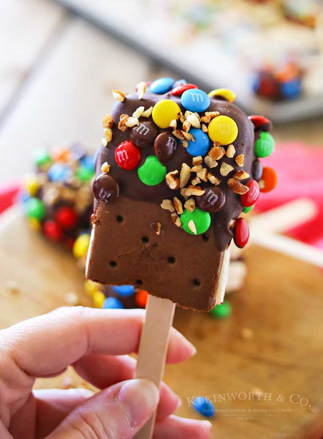 Ice Cream Sandwich Pops are an easy summer treat to make. Made with a simple ice cream sandwich, chocolate & decorations they are a perfect frozen treat. Make some for all of your celebrations, holidays & backyard BBQ's this summer. 