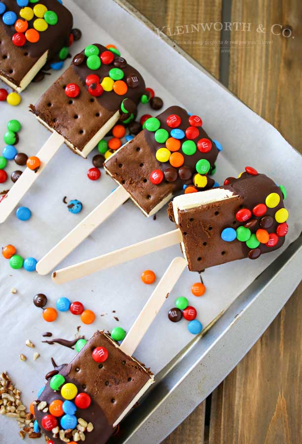 Ice Cream Sandwich Pops are an easy summer treat to make. Made with a simple ice cream sandwich, chocolate & decorations they are a perfect frozen treat. Make some for all of your celebrations, holidays & backyard BBQ's this summer. 