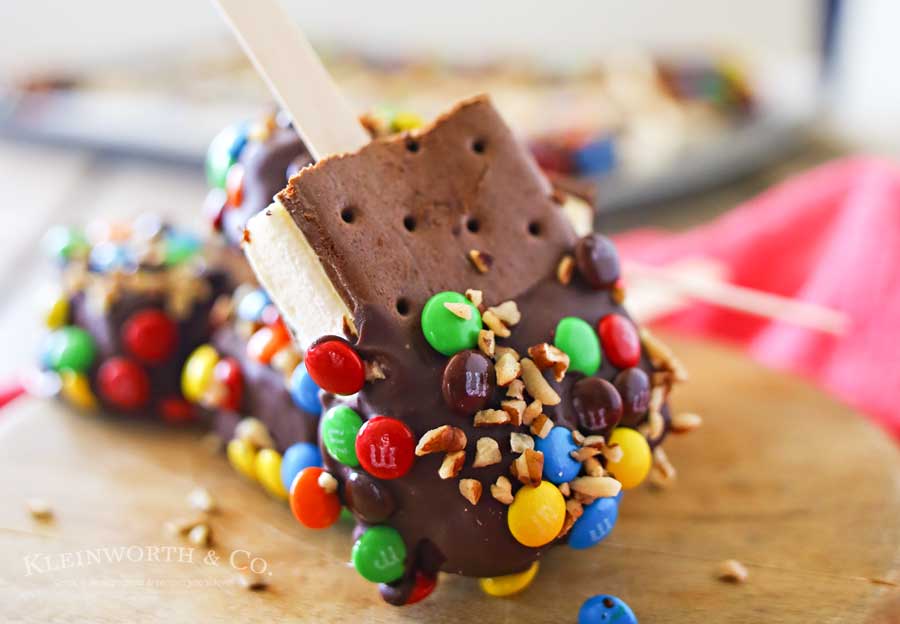 Ice Cream Sandwich Pops are an easy summer treat to make. Made with a simple ice cream sandwich, chocolate & decorations they are a perfect frozen treat. Make some for all of your celebrations, holidays & backyard BBQ's this summer. 